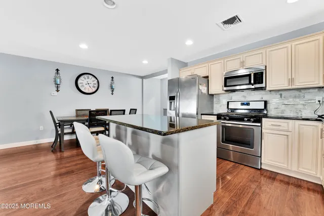 a kitchen with stainless steel appliances granite countertop a refrigerator a stove a sink a dining table and chairs