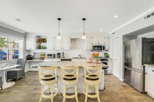 a kitchen with stainless steel appliances granite countertop a stove a sink dishwasher a refrigerator white cabinets with a dining table and chairs with wooden floor