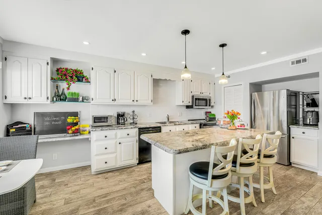 a kitchen with stainless steel appliances kitchen island granite countertop a sink a stove a refrigerator and white cabinets