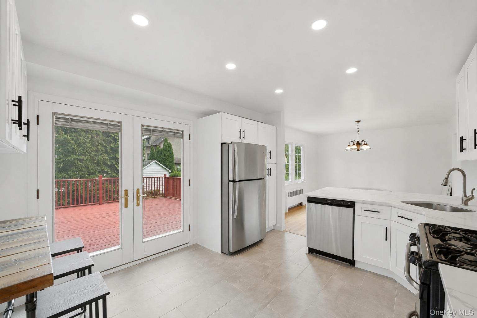 144 Bell Road Scarsdale, NY 10583 - Photo 15 of 49 Spacious kitchen featuring white cabinetry, stainless steel appliances, light-toned flooring, recessed lighting, and double glass doors opening to a red-stained deck
