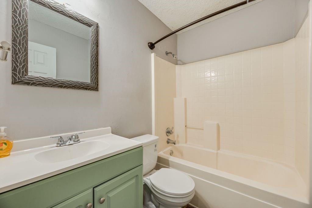 5610 Eagle Rock Road Arlington, TX 76017 - Photo 17 of 33 Bathroom featuring a tub/shower combination with tile surround, a vanity with a white countertop and integrated sink, a green-painted base cabinet with silver-tone hardware, and a framed mirror