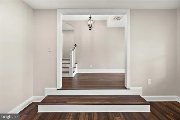 a view of an empty room with wooden floor kitchen view and a window