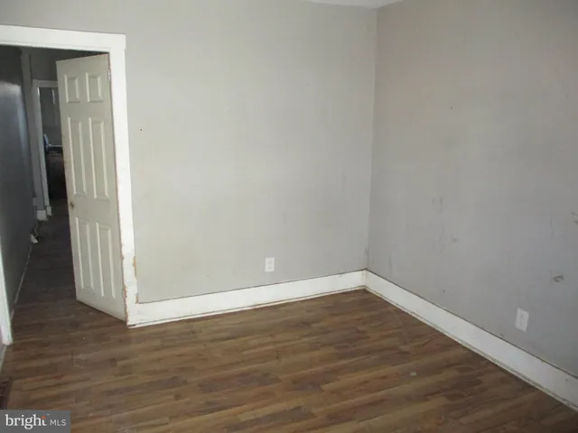 a view of an empty room with wooden floor and a hallway