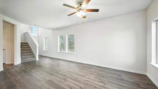 an empty room with wooden floor fan and windows
