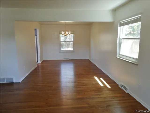 an empty room with wooden floor chandelier and windows