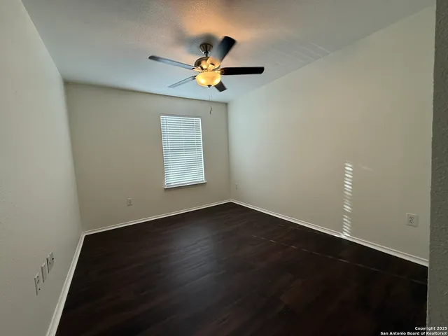 an empty room with wooden floor chandelier fan and windows