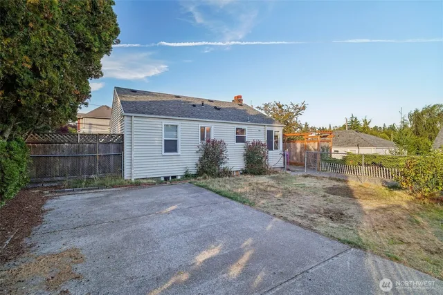 a view of a grey house with a yard and large tree
