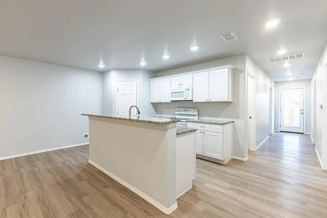 a view of kitchen with granite countertop refrigerator oven sink and white cabinets with wooden floor
