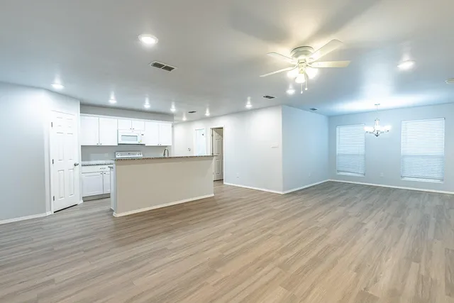an empty room with wooden floor and kitchen view