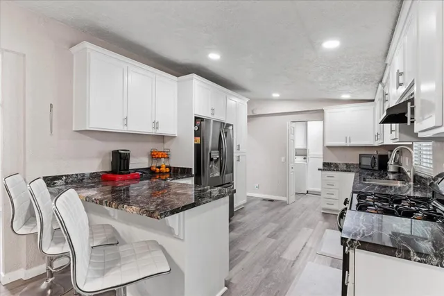 a kitchen with stainless steel appliances granite countertop a stove top oven a refrigerator a sink and white cabinets with wooden floor