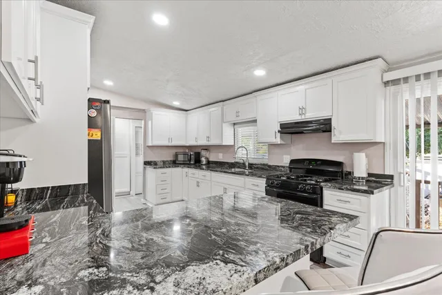 a kitchen with stainless steel appliances granite countertop a stove top oven a sink a refrigerator and white cabinets