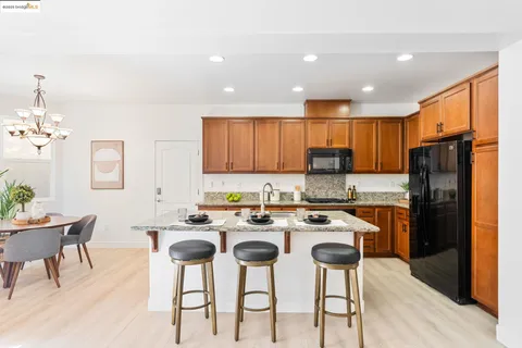 a kitchen with stainless steel appliances granite countertop a stove a refrigerator a sink dishwasher a dining table and chairs with wooden floor