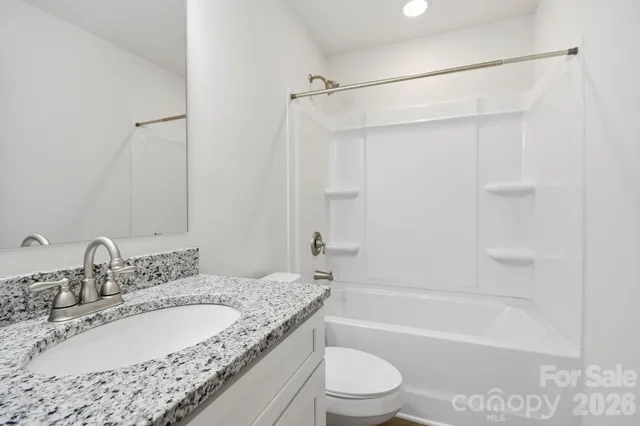 a bathroom with a granite countertop bathtub shower sink vanity and toilet
