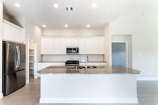 a kitchen with stainless steel appliances granite countertop a refrigerator a stove a sink a microwave and white cabinets