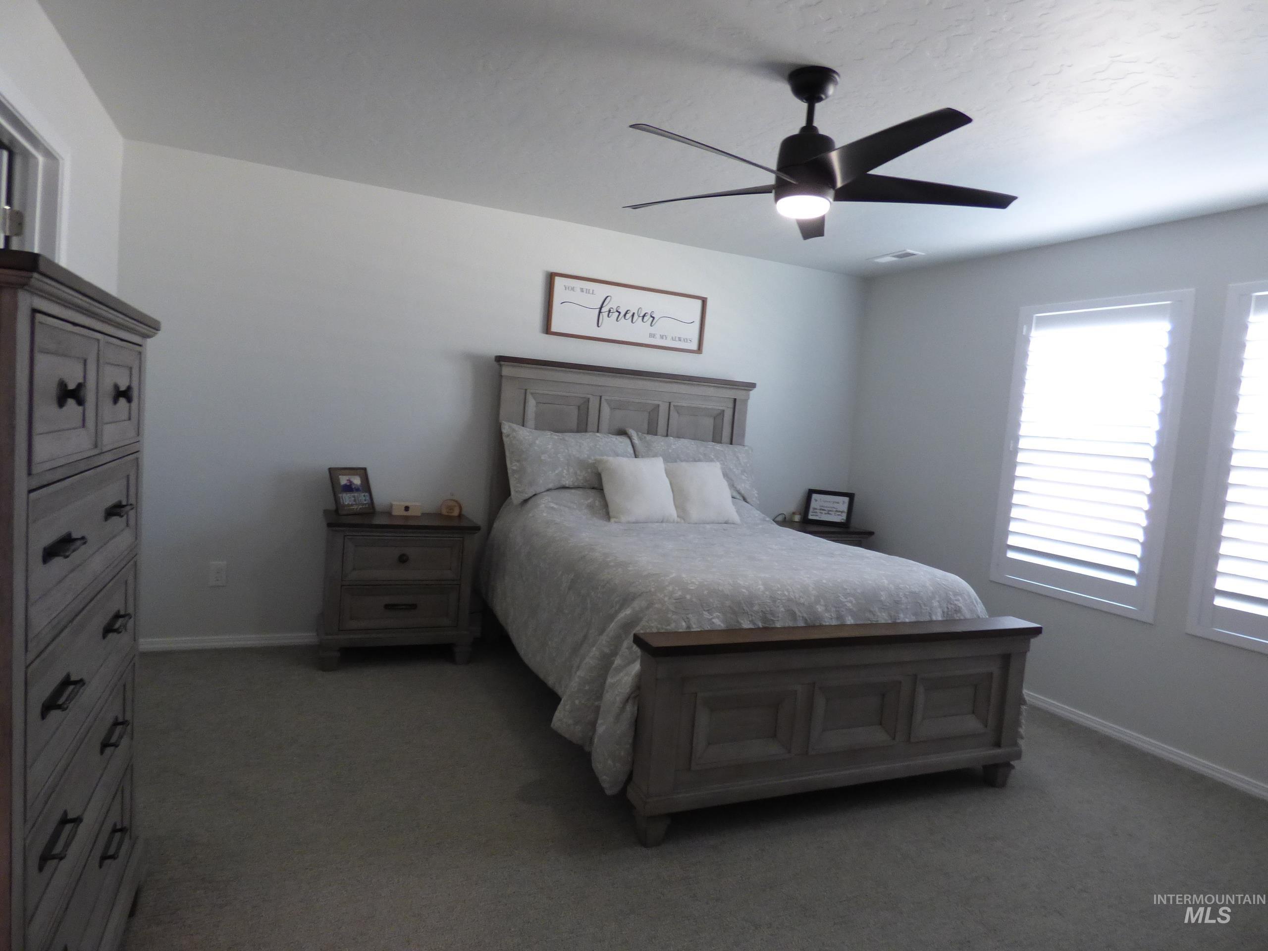 2708 East Buckaroo Drive Kuna, ID 83634 - Photo 16 of 48 Spacious room featuring light gray walls, dark gray carpet, two windows with white plantation shutters, and a ceiling fan with integrated lighting