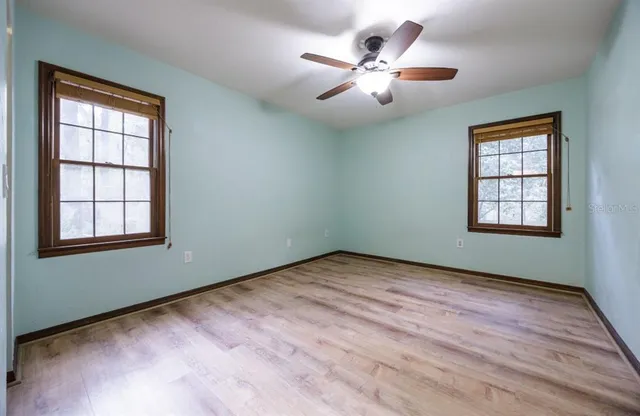 an empty room with wooden floor chandelier fan and windows