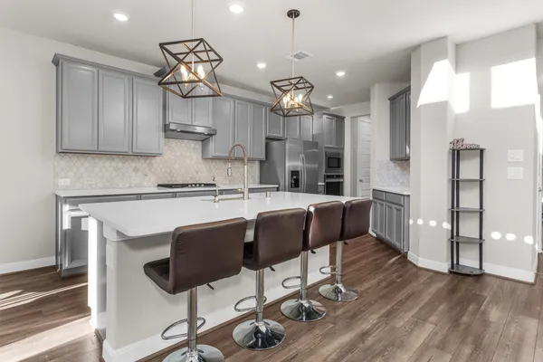 a kitchen with stainless steel appliances kitchen island granite countertop a refrigerator a stove top oven a sink dishwasher and a dining table with wooden floor
