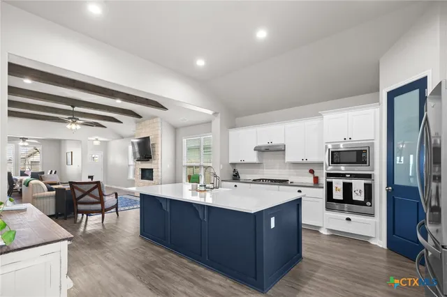 a large kitchen with a large counter top a sink stainless steel appliances and cabinets