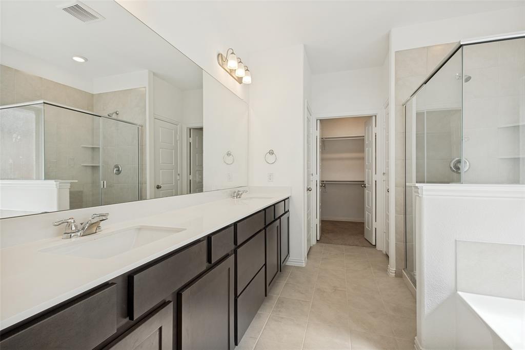 1448 Sun Gdn Way Justin, TX 76247 - Photo 10 of 15 Bathroom featuring a dual vanity with dark wood-finish cabinetry and white countertops, a large frameless mirror, and a glass-enclosed shower with tiled walls