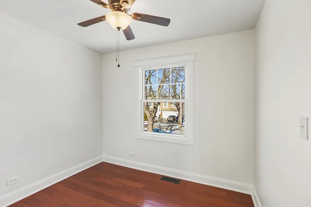 an empty room with wooden floor chandelier fan and windows