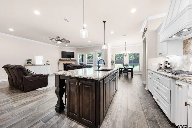 a kitchen with stainless steel appliances granite countertop a stove top oven a refrigerator a sink dishwasher and couches with wooden floor