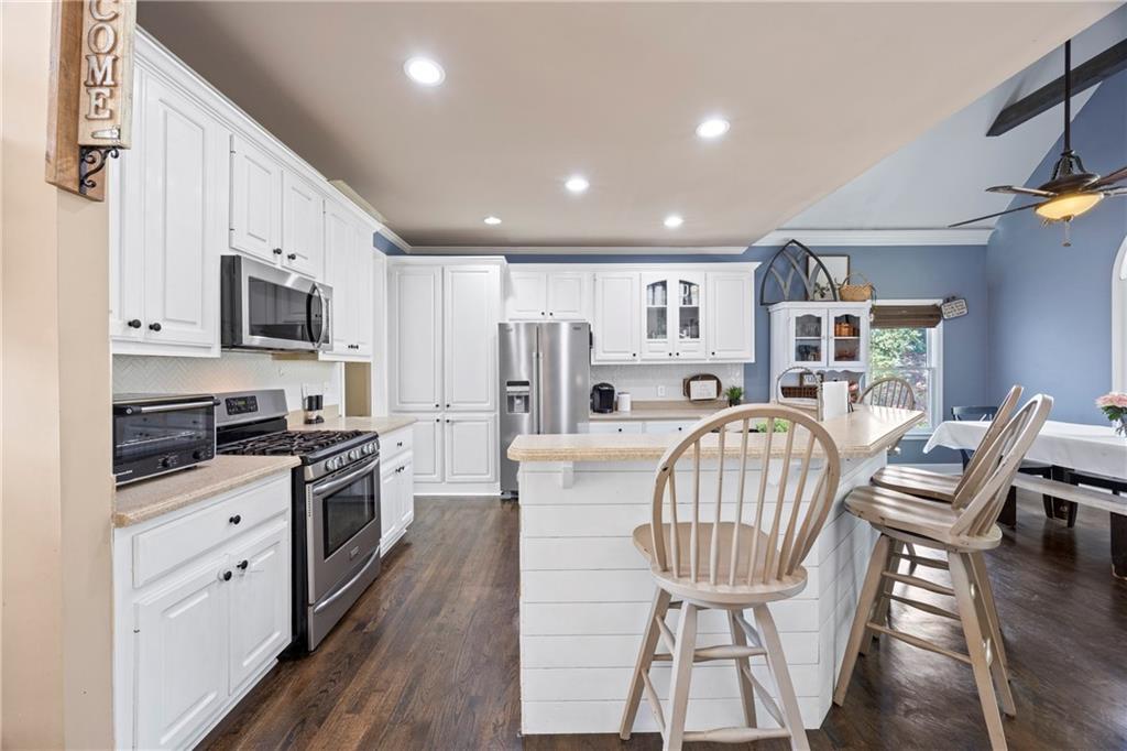 3420 Millwater Crossing Northeast Dacula, GA 30019 - Photo 13 of 54 a kitchen with stainless steel appliances granite countertop a stove top oven a refrigerator a kitchen island a dining table and chairs with wooden floor