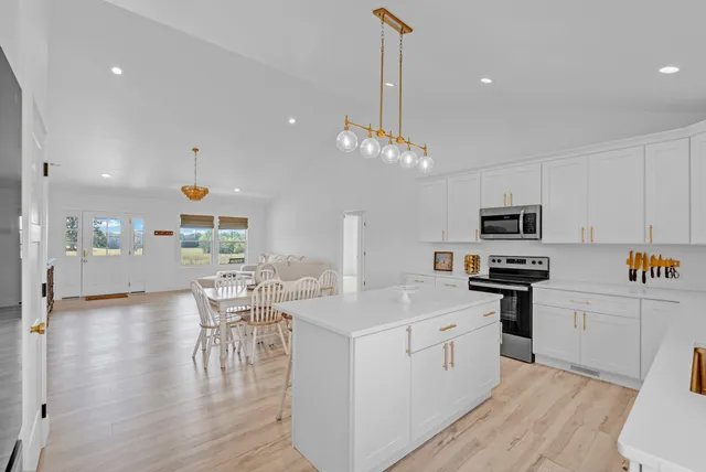 a kitchen with stainless steel appliances a microwave a stove a sink dishwasher a refrigerator and white cabinets with wooden floor