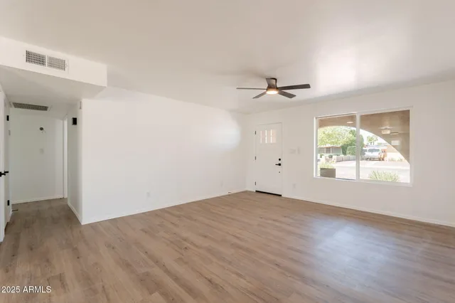 an empty room with wooden floor a ceiling fan and windows