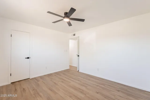 an empty room with wooden floor fan and windows