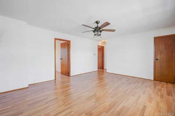 a view of an empty room with wooden floor and a ceiling fan