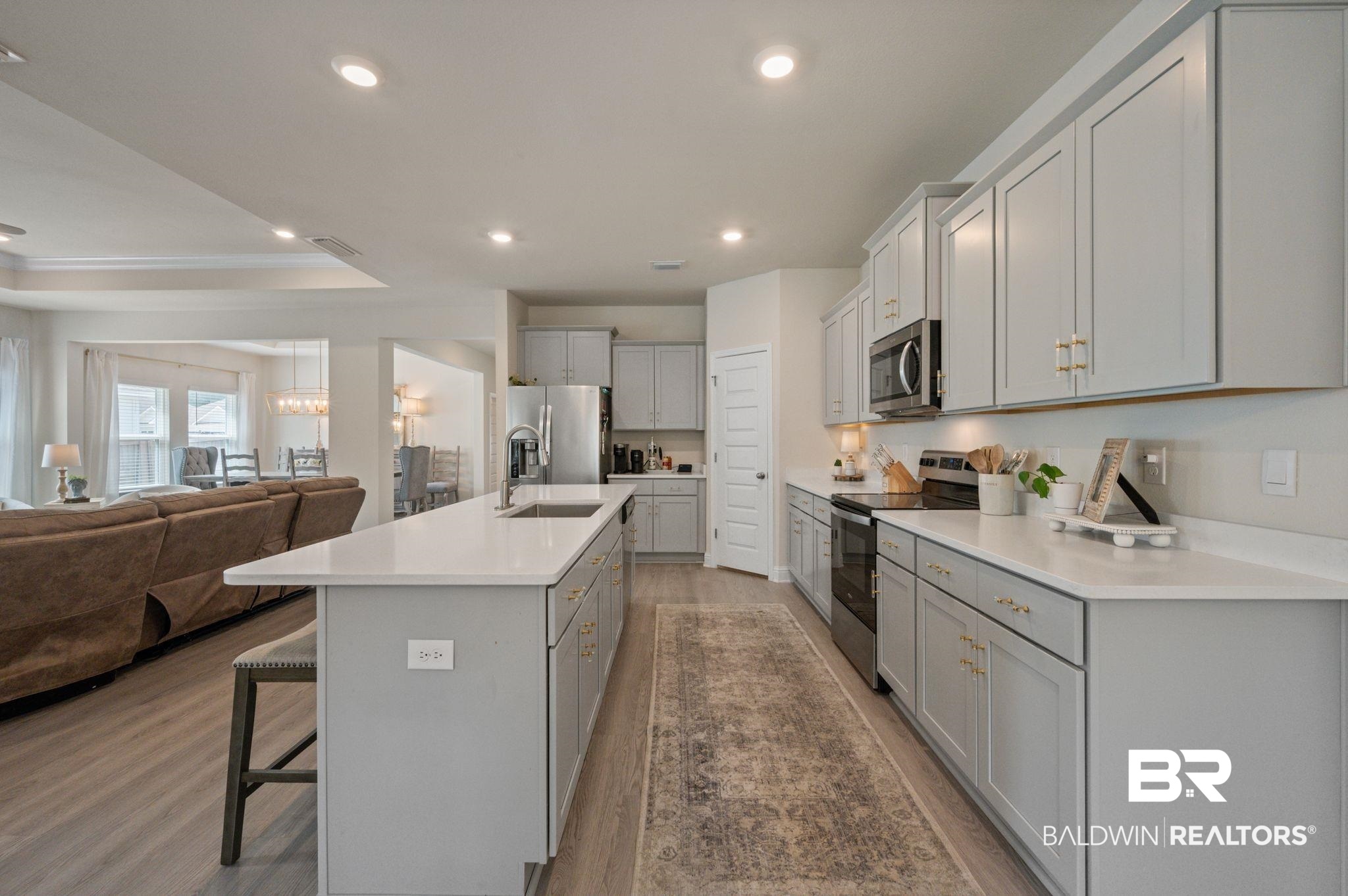 681 Calibre Street Fairhope, AL 36532 - Photo 20 of 56 Kitchen with a kitchen island with sink, a raised ceiling, a kitchen breakfast bar, wood-type flooring, and appliances with stainless steel finishes