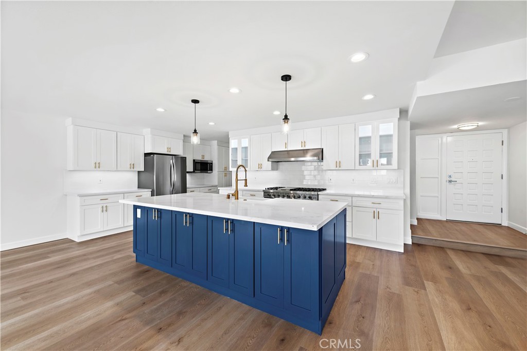 a kitchen with stainless steel appliances a sink a stove a refrigerator and white cabinets with wooden floor
