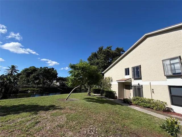 a view of a white house next to a yard with big trees