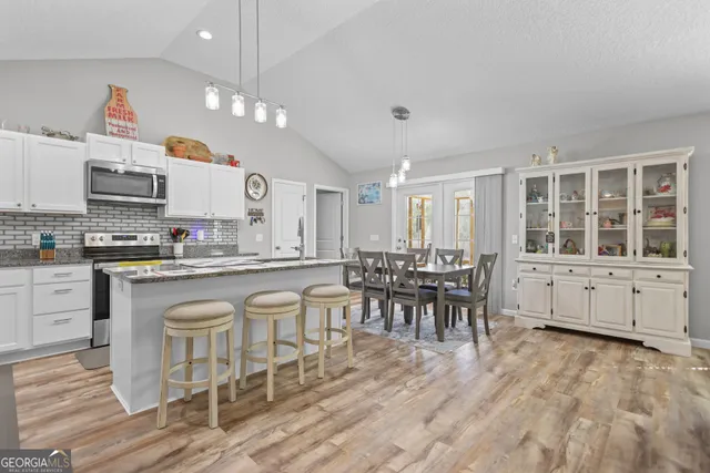 a kitchen with stainless steel appliances granite countertop a stove top oven a sink a dining table and chairs with wooden floor