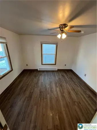 a view of an empty room with wooden floor and a ceiling fan