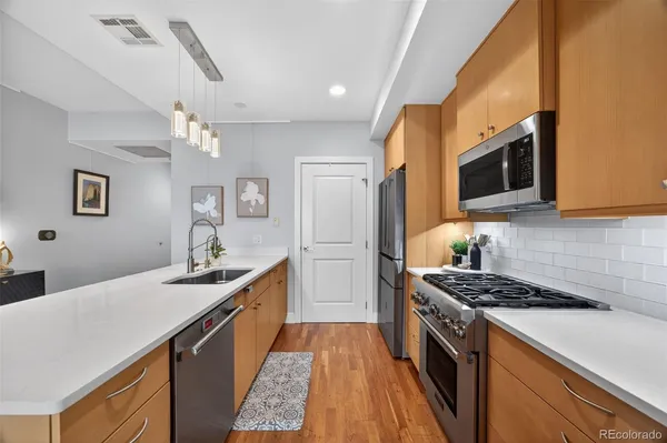 a kitchen with stainless steel appliances a stove a sink dishwasher a refrigerator white cabinets and wooden floor