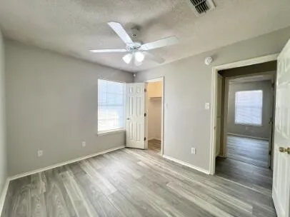 an empty room with wooden floor a ceiling fan and windows