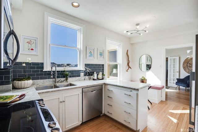 a kitchen with a sink dishwasher a stove and white cabinets with wooden floor
