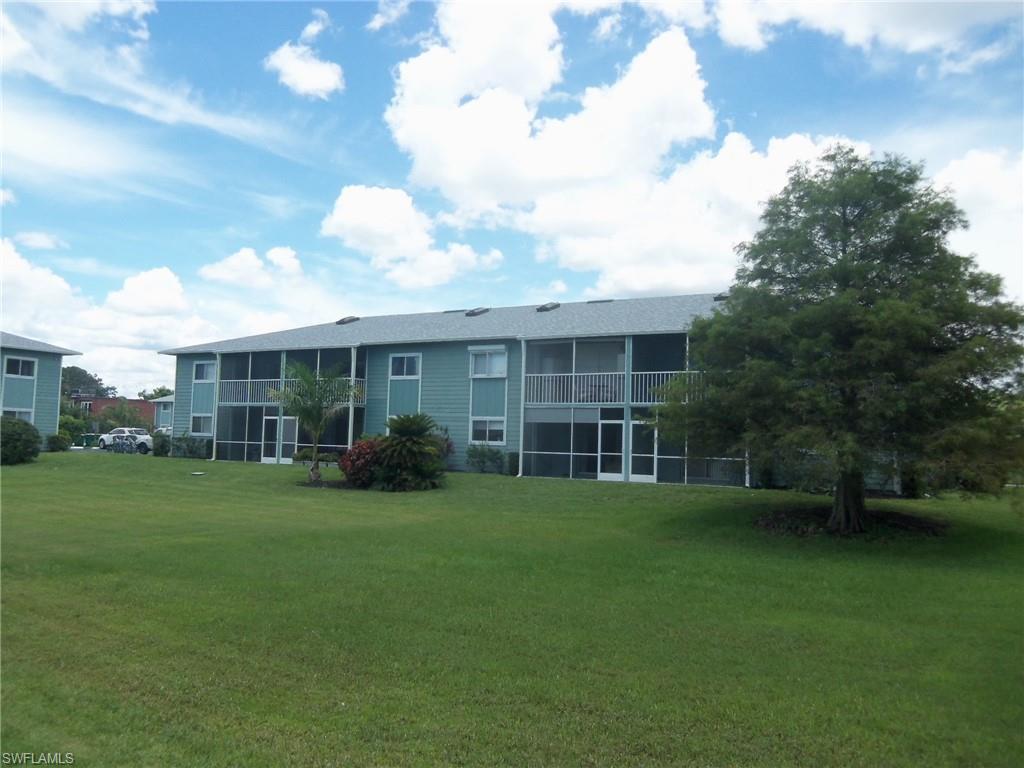 144 Cypress Way East, Unit 702 Naples, FL 34110 - Photo 16 of 18 a view of a house next to a big yard and large trees