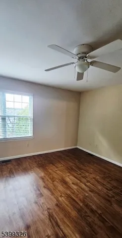 an empty room with wooden floor fan and windows