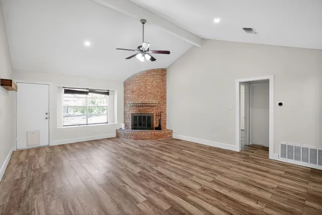 an empty room with wooden floor fireplace and windows