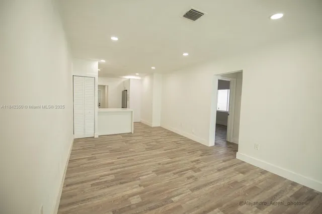 a view of an empty room with wooden floor and a kitchen