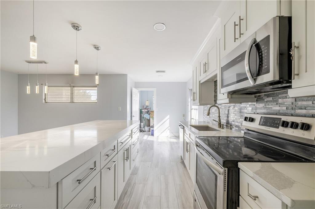 339 Beachwood Road Lehigh Acres, FL 33936 - Photo 1 of 32 Kitchen with stainless steel appliances, light stone counters, pendant lighting, white cabinets, and a spacious island