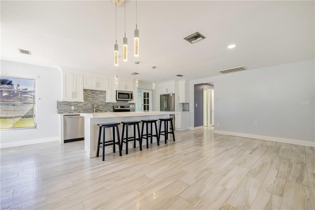 339 Beachwood Road Lehigh Acres, FL 33936 - Photo 2 of 32 Kitchen featuring a kitchen breakfast bar, hanging light fixtures, a kitchen island, backsplash, and stainless steel appliances
