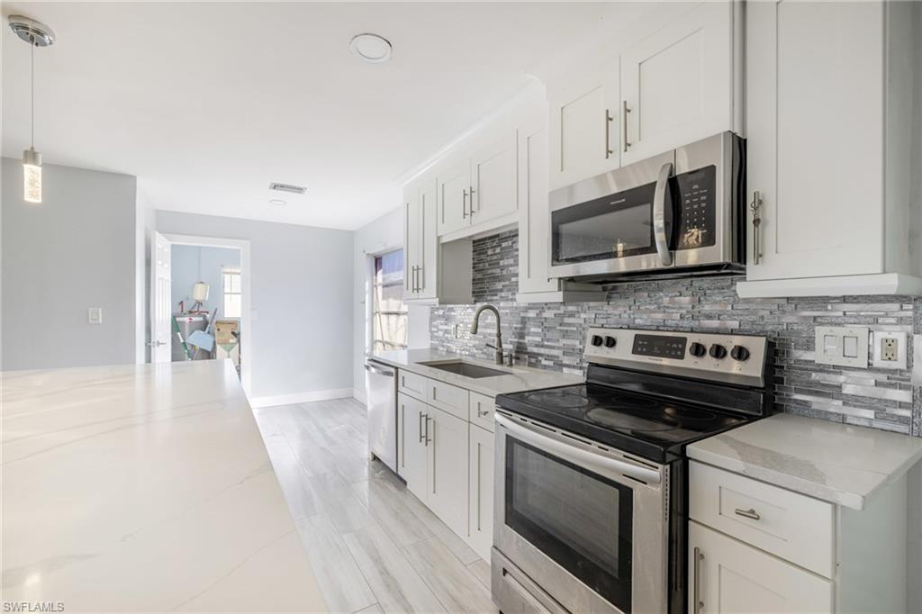 339 Beachwood Road Lehigh Acres, FL 33936 - Photo 3 of 32 Kitchen with stainless steel appliances, white cabinetry, decorative light fixtures, tasteful backsplash, and light stone counters