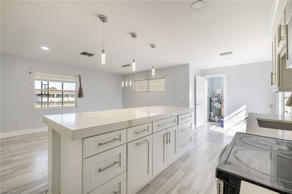 339 Beachwood Road Lehigh Acres, FL 33936 - Photo 4 of 32 Kitchen featuring a center island, black range with electric stovetop, hanging light fixtures, light stone countertops, and white cabinets