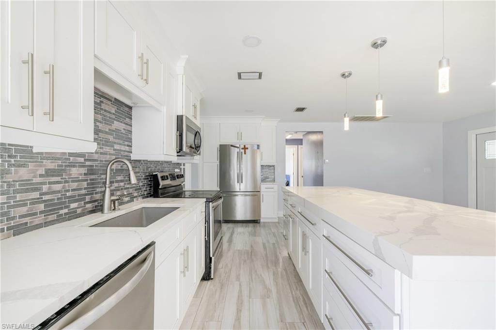 339 Beachwood Road Lehigh Acres, FL 33936 - Photo 5 of 32 Kitchen featuring appliances with stainless steel finishes, tasteful backsplash, a center island, hanging light fixtures, and light stone countertops