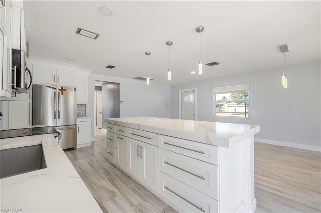 339 Beachwood Road Lehigh Acres, FL 33936 - Photo 6 of 32 Kitchen with stainless steel appliances, decorative light fixtures, white cabinetry, light wood-style flooring, and a center island