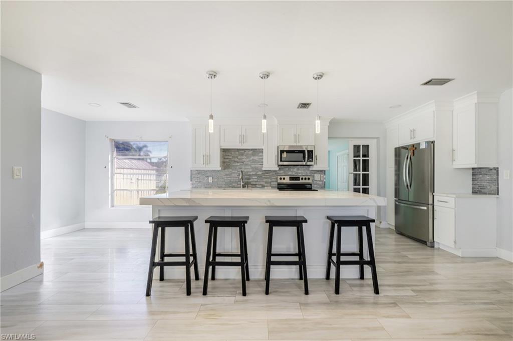339 Beachwood Road Lehigh Acres, FL 33936 - Photo 8 of 32 Kitchen with appliances with stainless steel finishes, decorative light fixtures, a breakfast bar, white cabinetry, and decorative backsplash