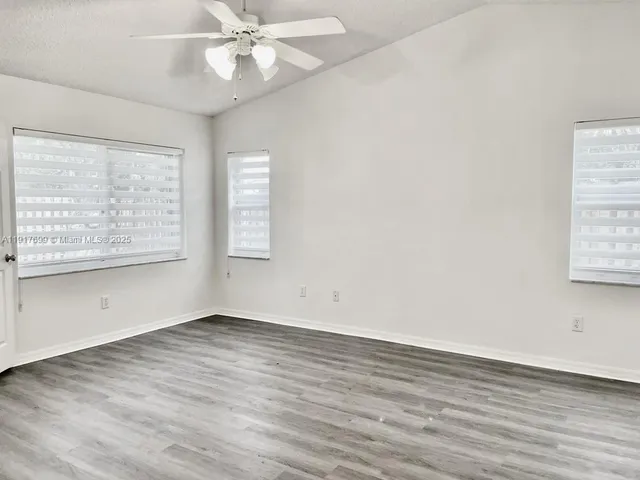 an empty room with wooden floor fan and windows
